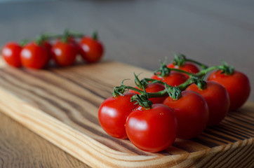 A branch of cherry tomatoes on wooden cutting board