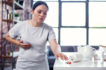 Flu spreading. Asian upset woman looking at pills and touching belly