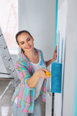 I am inspired. Cheerful dark-haired woman redecorating her room and holding a roller