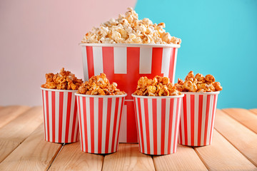 Cups with tasty popcorn on table against color background
