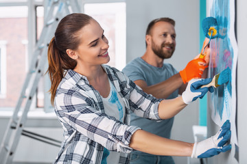 Our work. Inspired dark-haired painter painting the wall and working with her colleague