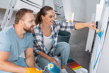Our love. Alert loving woman painting a heart and her beloved man sitting near her
