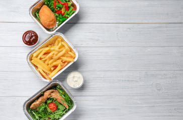 Foil containers with delicious food on wooden background
