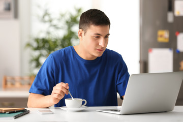 Young man drinking coffee while working with laptop in home office