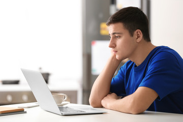 Young man working with laptop at table in home office