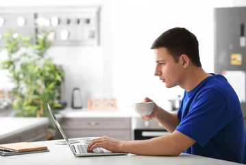 Young man drinking coffee while working with laptop in home office