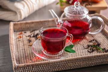 Tray with glass pot and cup of delicious red tea on table