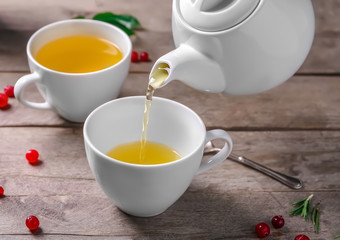 Pouring green tea into ceramic cup on wooden table