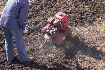 Worker with a machine cultivator digs the soil in the garden