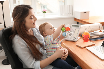 Young mother holding baby while working in office