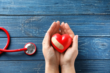 Woman holding red heart with medical plaster on wooden background. Health care concept