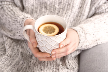 Young woman holding mug of hot aromatic tea with lemon, closeup