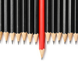 Red pencil standing out from crowd of plenty identical black fellows on white table. Leadership,...