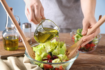 Woman pouring olive oil into bowl with fresh vegetable salad on table