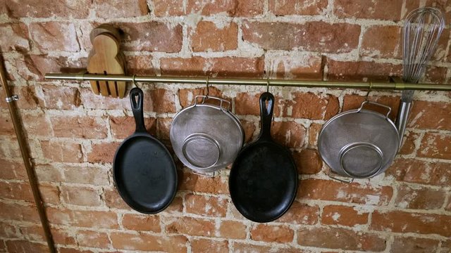 Kitchen interior. Panorama of cast iron frying pans, sieves, whisk, wooden cutting boards on brick wall background. 4K