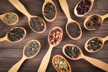 Different sorts of tea in spoons on wooden background, flat lay