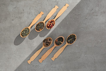 Different sorts of tea in spoons on light background, flat lay