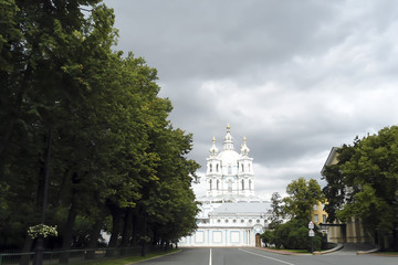 road past the park to the elegant white church, Smolny Convent site, Saint Peterburg (Russia); stormy clouds in the sky