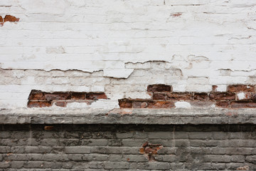 An old brick wall with cracks on the white and dark plaster.