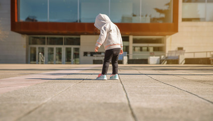 Back view of little girl with hoodie looking her new sneakers in a city square on a sunny day