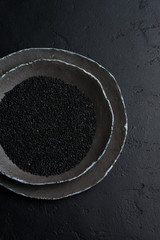Black sesame seeds in black ceramic plates on a dark old vintage background. Rustic style. Top view.
