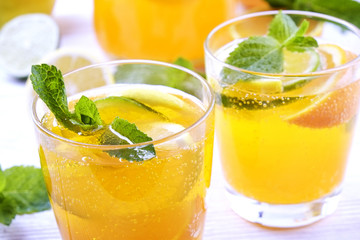 Two glasses & pitcher bottle of homemade refreshing lemonade with slices of organic ripe lemon, orange and lime, mint & ice on rustic white wooden table background. Close up, top view, copy space.