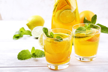 Two glasses & pitcher bottle of homemade refreshing lemonade with slices of organic ripe lemon, orange and lime, mint & ice on rustic white wooden table background. Close up, top view, copy space.