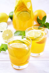 Two glasses & pitcher bottle of homemade refreshing lemonade with slices of organic ripe lemon, orange and lime, mint & ice on rustic white wooden table background. Close up, top view, copy space.