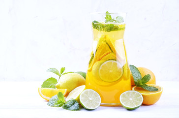 Two glasses & pitcher bottle of homemade refreshing lemonade with slices of organic ripe lemon, orange and lime, mint & ice on rustic white wooden table background. Close up, top view, copy space.