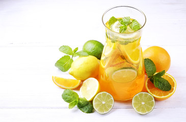 Two glasses & pitcher bottle of homemade refreshing lemonade with slices of organic ripe lemon, orange and lime, mint & ice on rustic white wooden table background. Close up, top view, copy space.