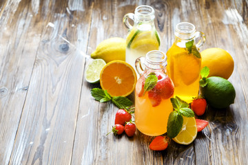 Three vintage bottles of fresh ice cold lemonade, different taste drinks w/ lemon, orange, grapefruit, lime, mint leaves & strawberry on grunged wooden table background. Top view, copy space, close up