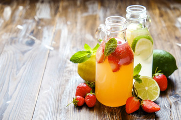 Three vintage bottles of fresh ice cold lemonade, different taste drinks w/ lemon, orange, grapefruit, lime, mint leaves & strawberry on grunged wooden table background. Top view, copy space, close up