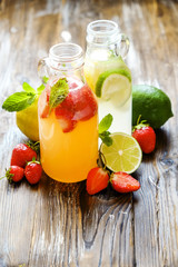 Three vintage bottles of fresh ice cold lemonade, different taste drinks w/ lemon, orange, grapefruit, lime, mint leaves & strawberry on grunged wooden table background. Top view, copy space, close up