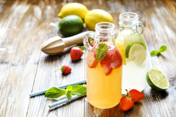 Three vintage bottles of fresh ice cold lemonade, different taste drinks w/ lemon, orange, grapefruit, lime, mint leaves & strawberry on grunged wooden table background. Top view, copy space, close up