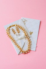 Wedding concept. Invitation cars and pearl necklace on a pink ba