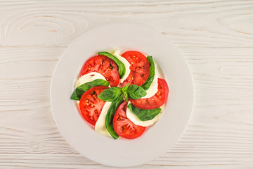 Italian caprese, tomatoes, mozzarella and basil, on a wooden background