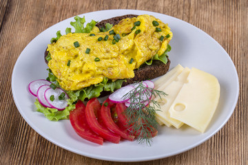 Egg omelette on a piece of black bread with red tomatoes, cheese and radish on a wooden table, close up