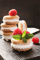 Ice cream cookie sandwiches with cocco and raspberries on wooden background.