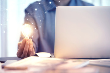 Happy woman holding light bulb while using on laptop, New ideas and creativity concept.