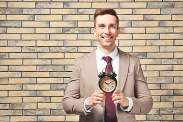 Successful businessman with alarm clock against brick wall. Time management concept
