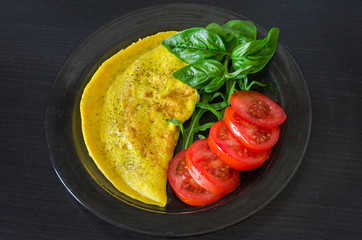 Omelette on a plate with rucola, basil and tomato