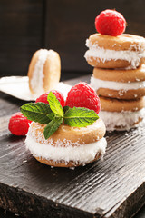 Ice cream cookie sandwiches with cocco and raspberries on wooden background.