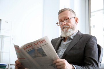 Senior man reading newspaper in office