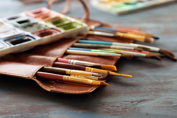 Bag with paint brushes and watercolors on wooden table