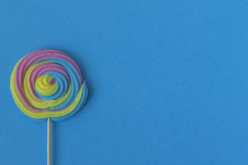 Creative view of colorful, handmade swirl lollipop in summer colors on blue paper background. Minimalism. Abstraction.