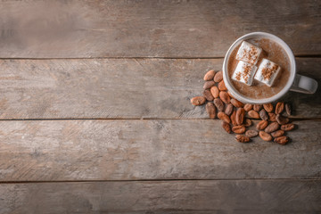 Cup of delicious cocoa drink with marshmallows and beans on wooden table