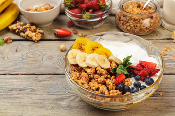 Bowl of homemade granola with yogurt and fresh berries on wooden background