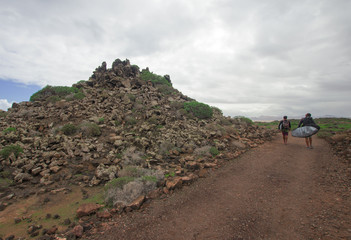 two surfers walk a difficult path to reach the ocean.Fuerteventura, Canary Islands