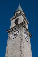 Light grey tower bell of the main church seen from below with blue sky in Pinzolo