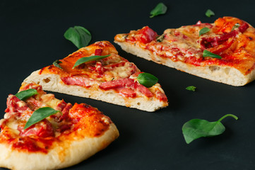 Three slices salami mozarella pizza black background. Close up.
